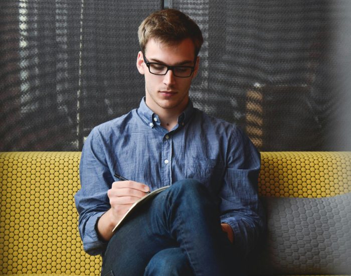 Person in Blue Denim Jacket Sitting on Chair While Writing